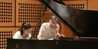 A student at the piano with their teacher