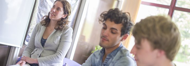 Two students chatting at a table covered in notes with another student sat behind them.
