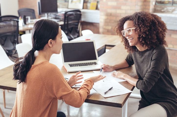 Two woman sitting at a desk discussing paperwork
