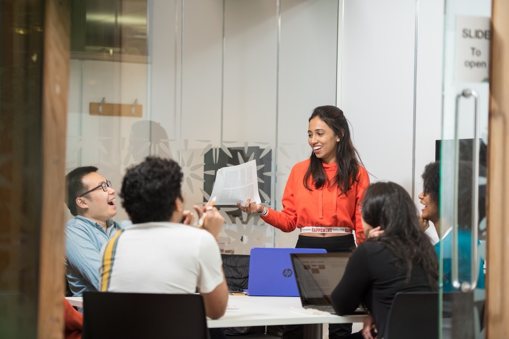 Woman standing in a conference room with people sitting at the table around her