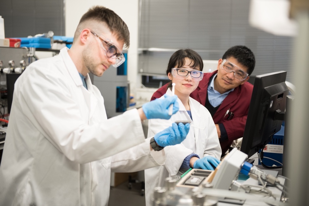 Three researchers, two are looking at the other carrying out an experiment
