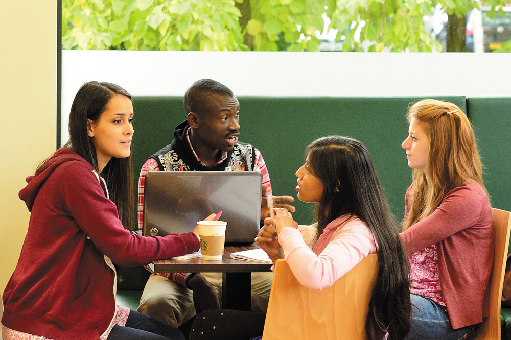 Group of four students sitting around a table with laptop, chatting