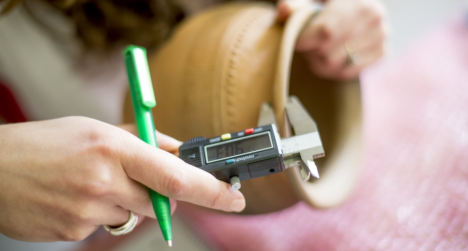 Postgraduate student holding a green pen while using measuring callipers on a pot for pottery cataloguing