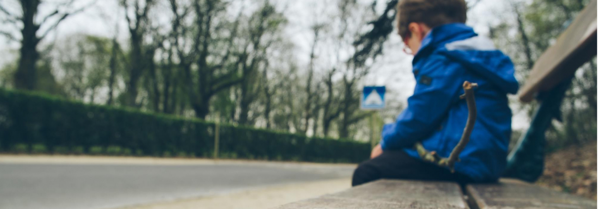 Little boy sat on a bench outside holding a stick